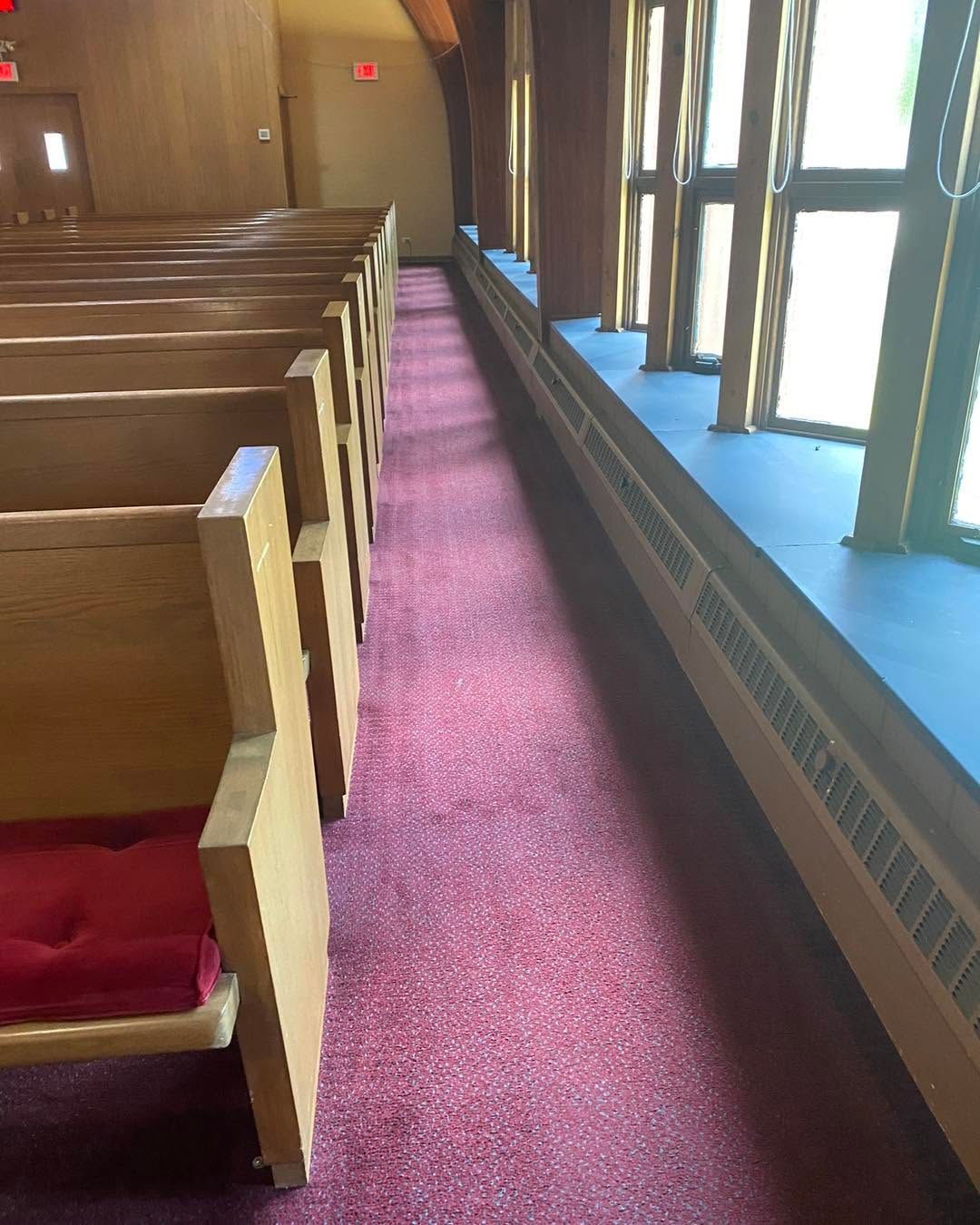 Empty church pews beside a purple carpet aisle and blue carpeted window ledge.