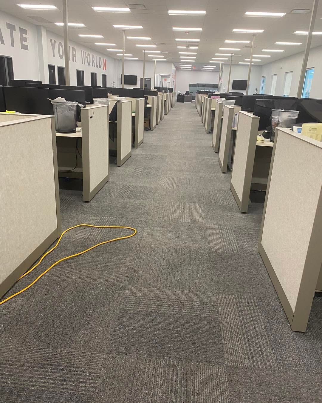 Office cubicle aisle with rows of desks, carpeted floor, and a yellow cable lying across the walkway.
