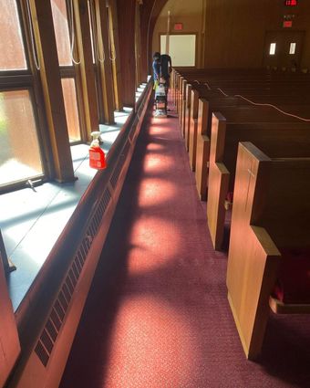 Long church pew aisle with sunlight on red carpet and a person in the distance