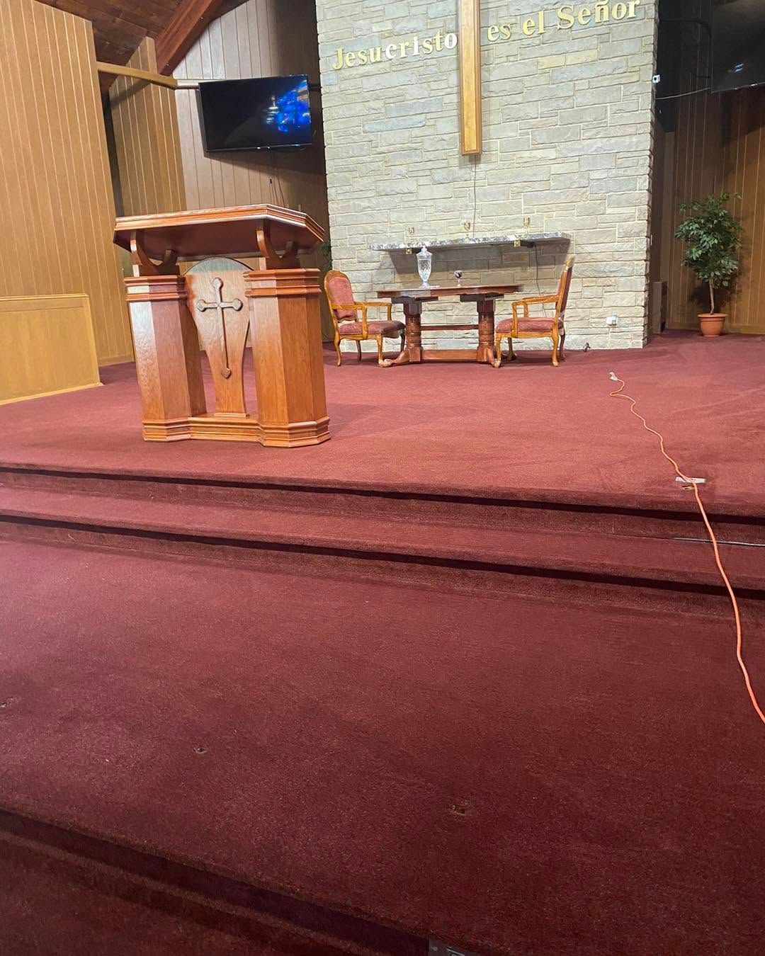 Church sanctuary with red carpet, pulpit, chairs, and a large cross on the wall.