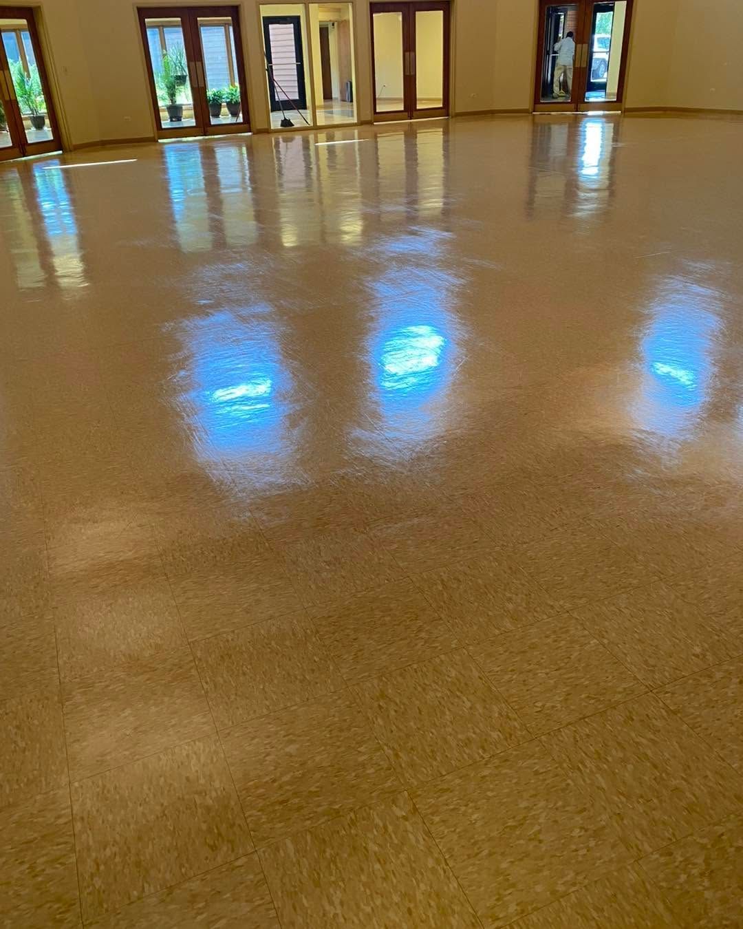 Empty polished hall with tan floor and glass doors, reflecting blue light from windows.