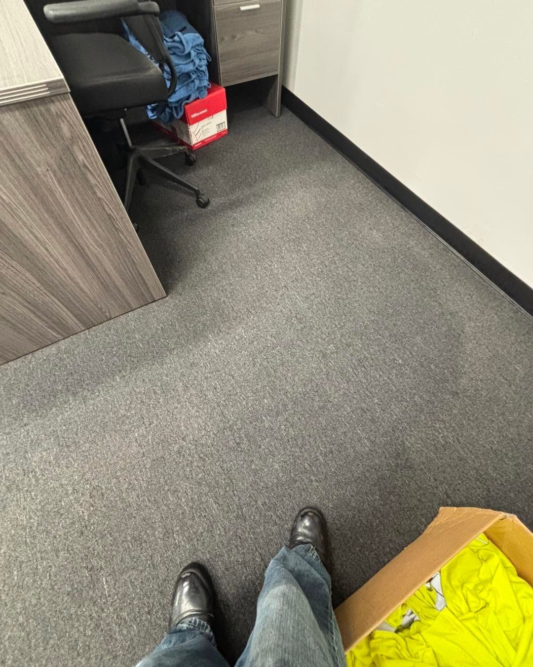 Standing in an office hallway, looking toward a chair, a red box, and a bright yellow bag on the floor