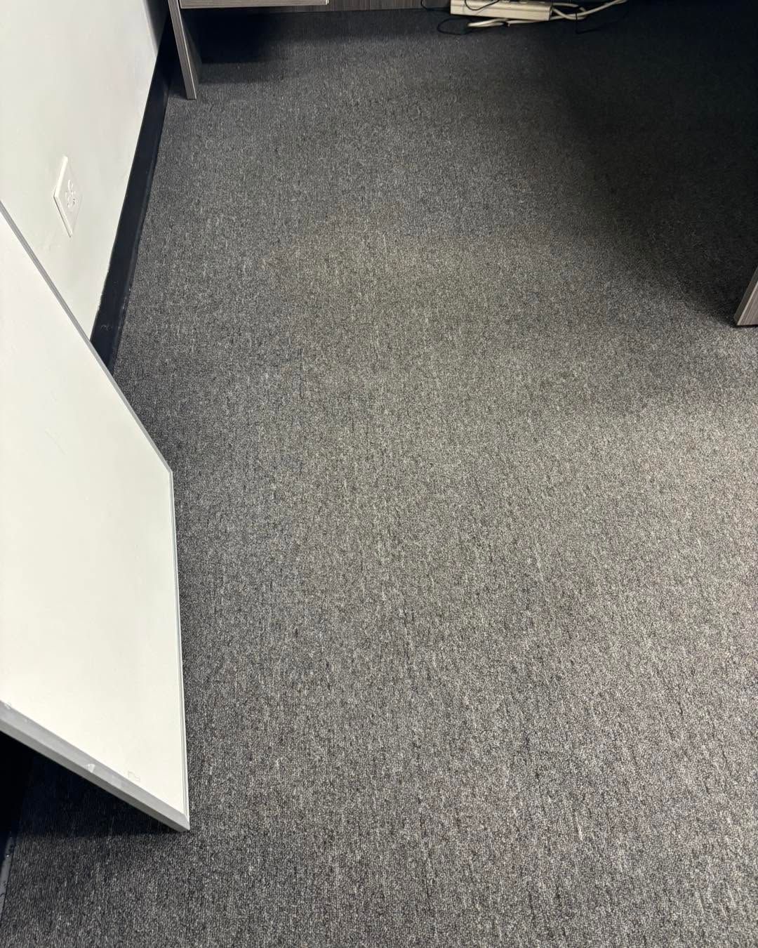 Empty office corner with gray carpet and white walls, viewed from a doorway