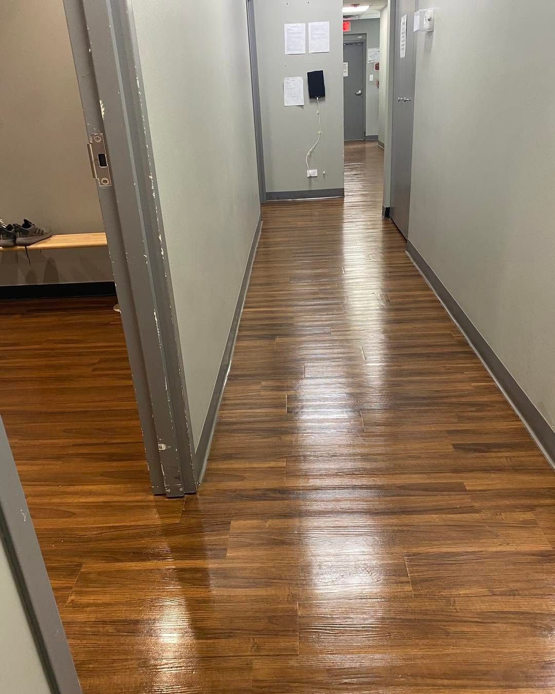 Narrow hallway with glossy wood floors and gray walls, leading to a doorway at the end.