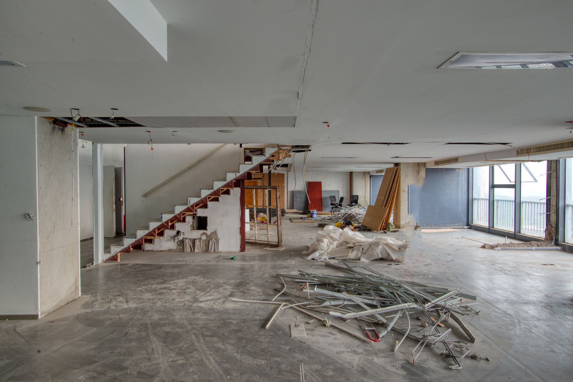 Interior space under renovation, with exposed walls, stairs, and debris on the floor.