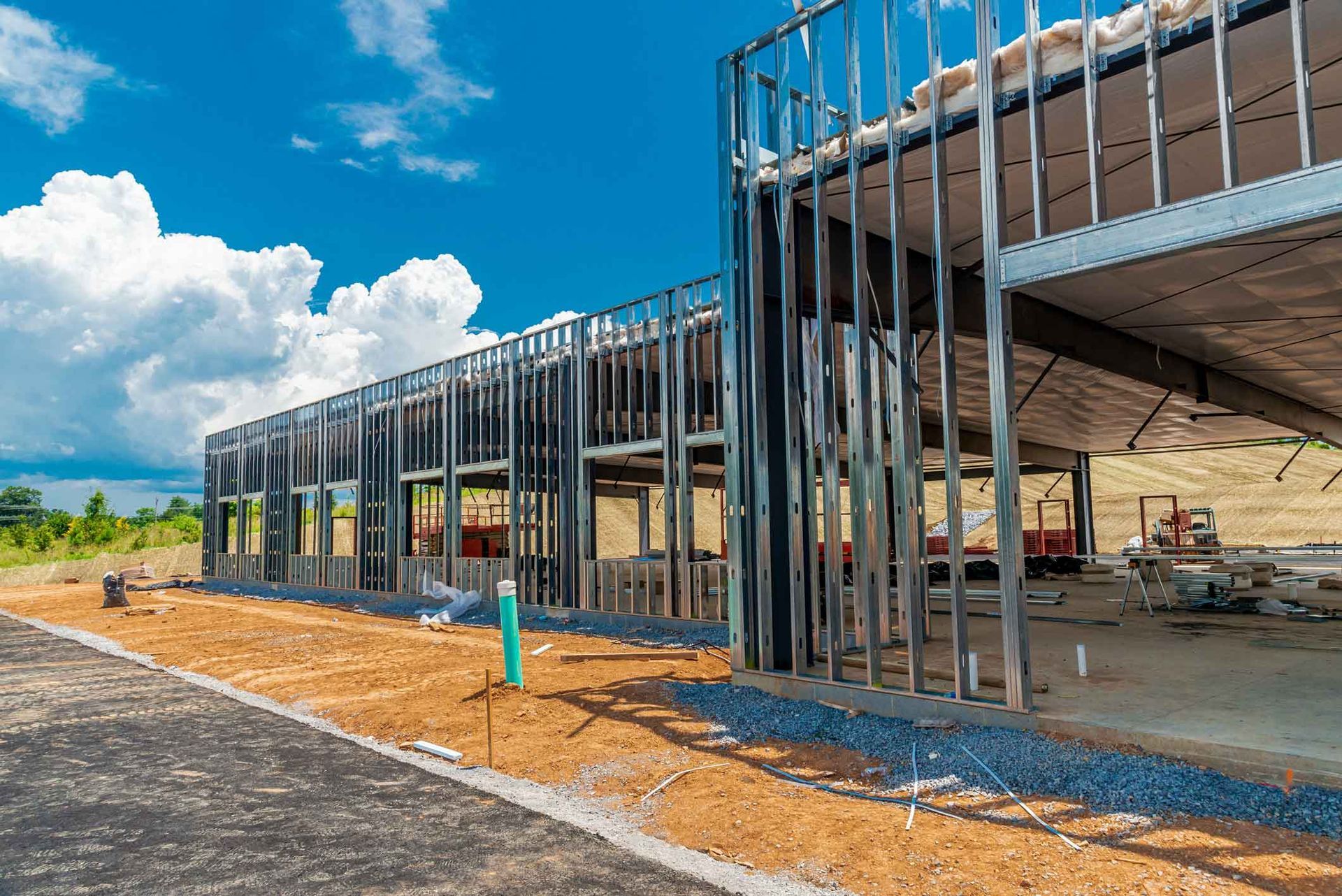 Steel frame of a building under construction against a bright blue sky with clouds.