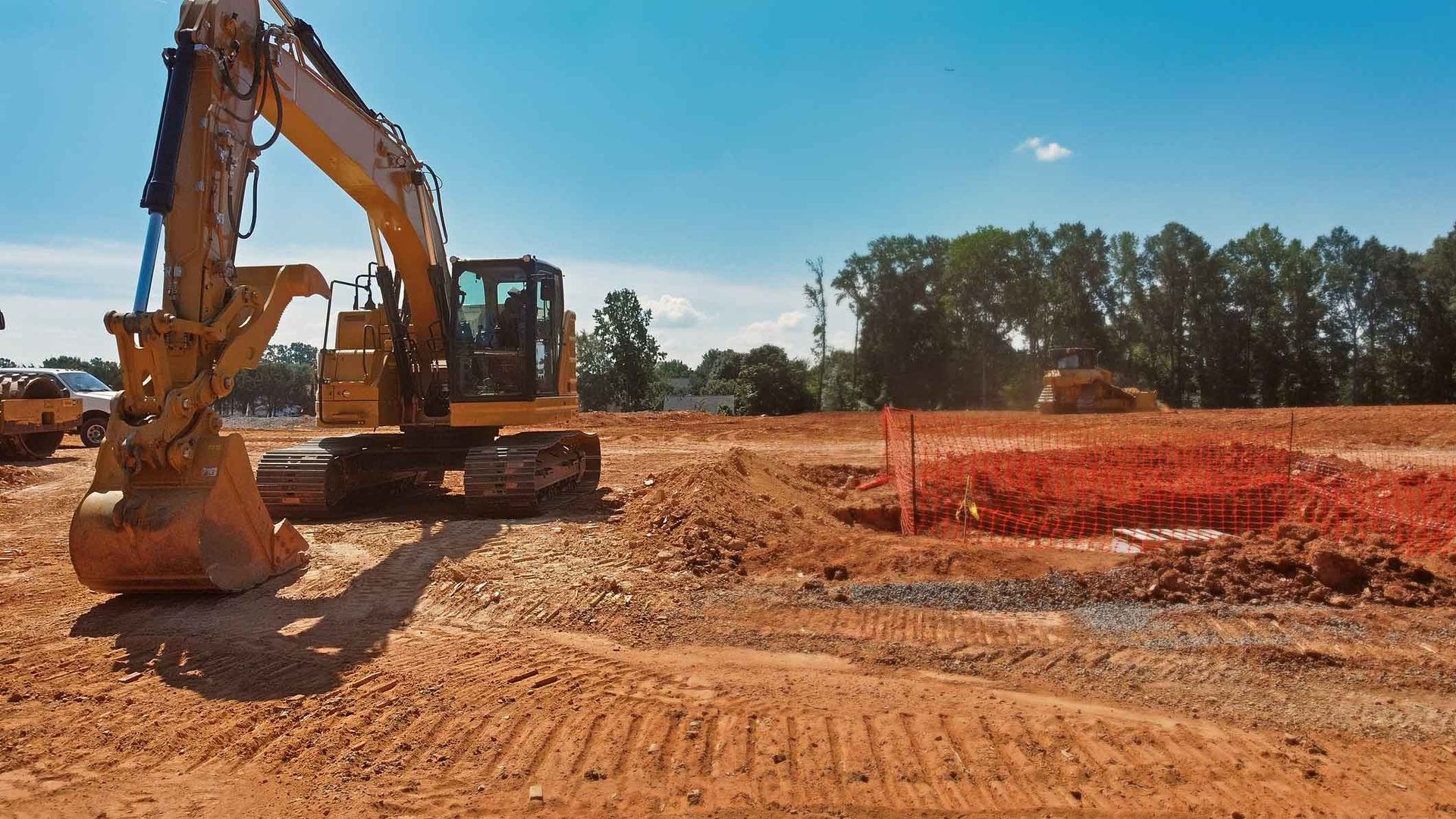 Construction site with excavator and red dirt under blue sky.