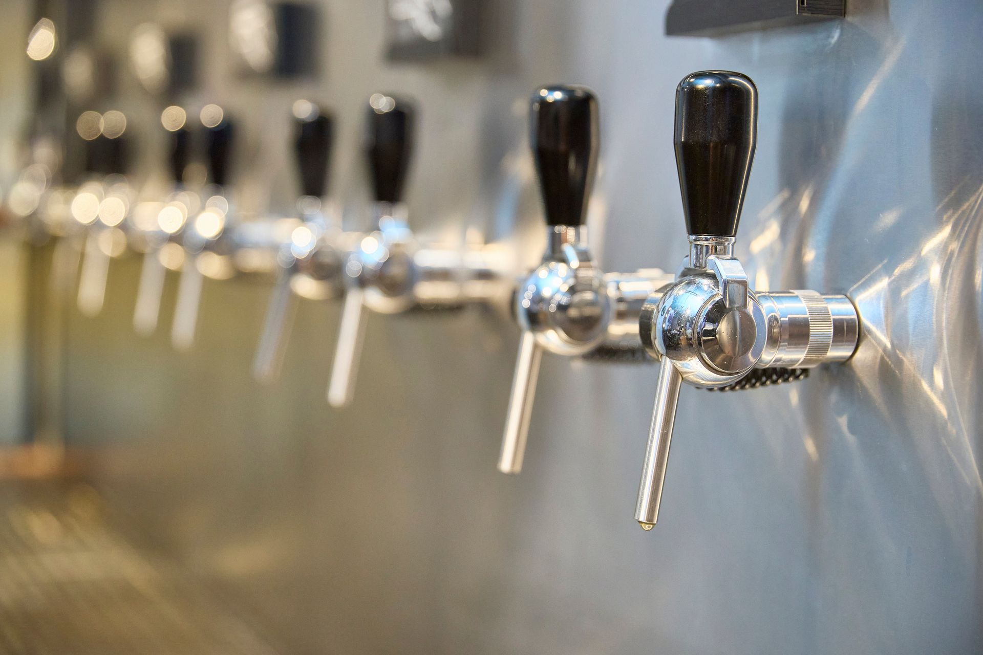 Row of Beer Taps With Black Handles on a Stainless Steel Bar Counter — Nauticool Refrigeration & Air Conditioning in Cannonvale, QLD