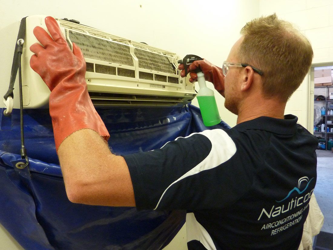 A Man Wearing Red Gloves is Cleaning an Air Conditioner — Nauticool Refrigeration & Air Conditioning in Cannonvale, QLD