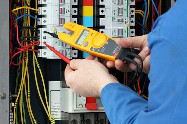 A Man is Working on an Electrical Box With a Clamp Meter — Nauticool Refrigeration & Air Conditioning in Cannonvale, QLD
