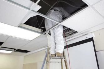 A Man is Standing on a Ladder Looking Up at the Ceiling — Nauticool Refrigeration & Air Conditioning in Cannonvale, QLD