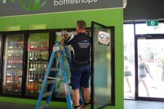 A Man on a Ladder in Front of a Refrigerator in a Store — Nauticool Refrigeration & Air Conditioning in Cannonvale, QLD