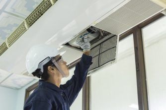 A Man is Working on an Air Conditioner in a Room — Nauticool Refrigeration & Air Conditioning in Cannonvale, QLD