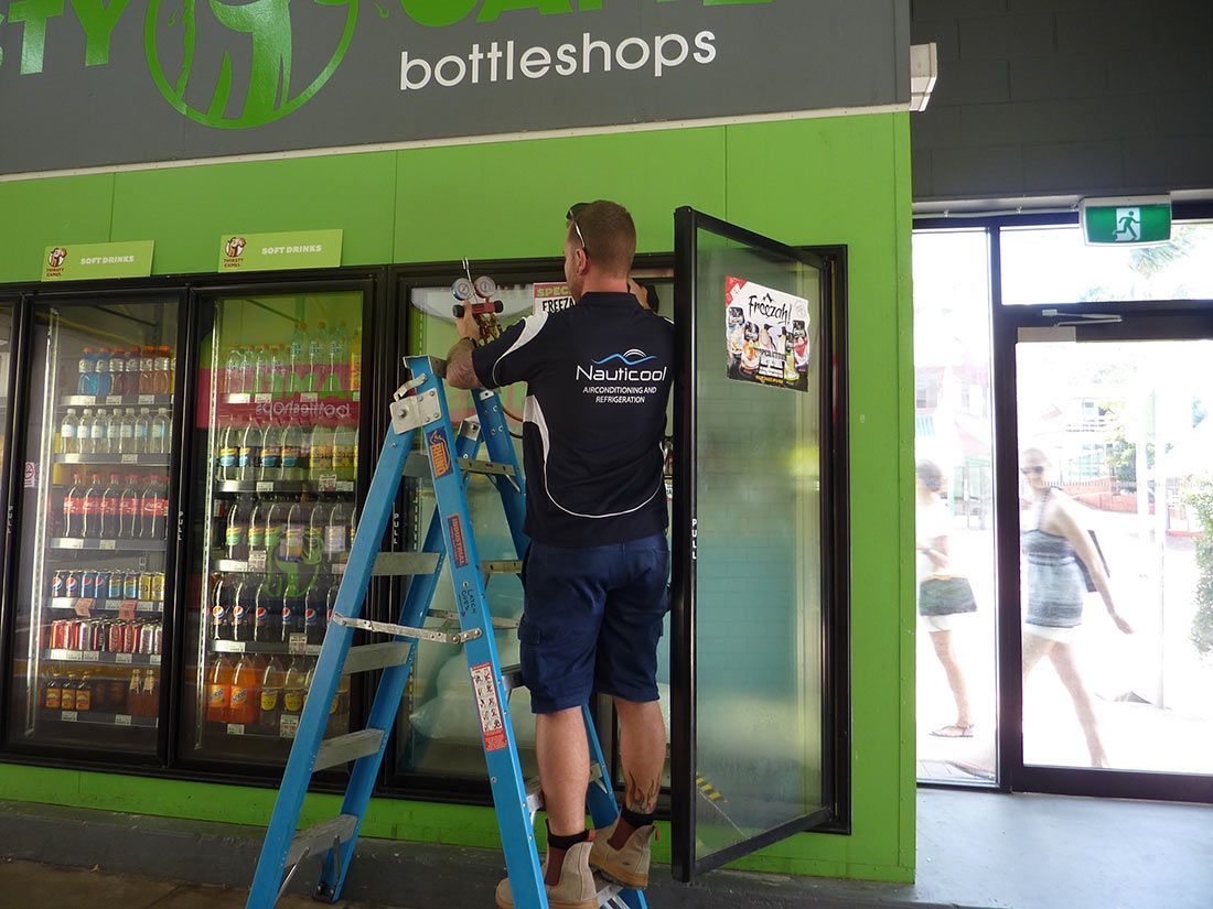 A Man Standing on a Ladder in Front of a Bottle Shop — Nauticool Refrigeration & Air Conditioning in Cannonvale, QLD