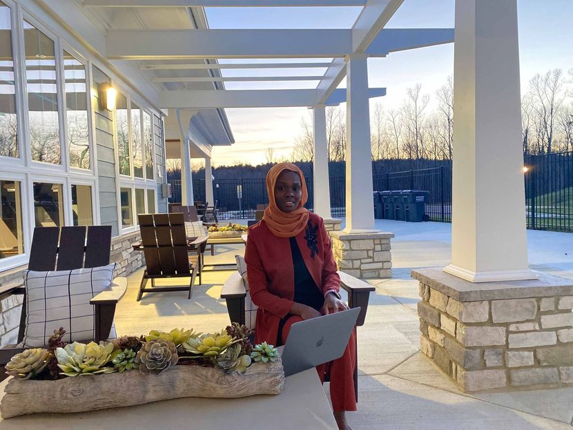 Person in a red coat standing on a snow-covered patio with chairs, stone planters, and a laptop.