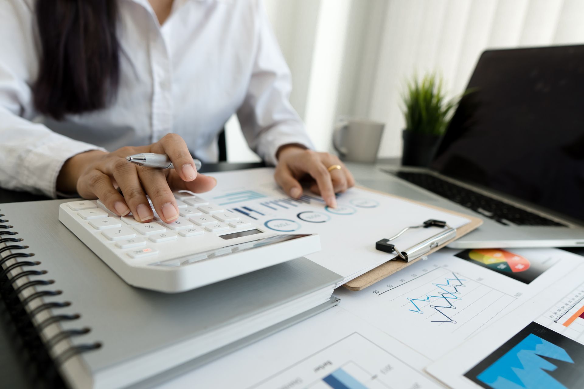 Person reviewing charts and notes on a desk with a laptop and notebook