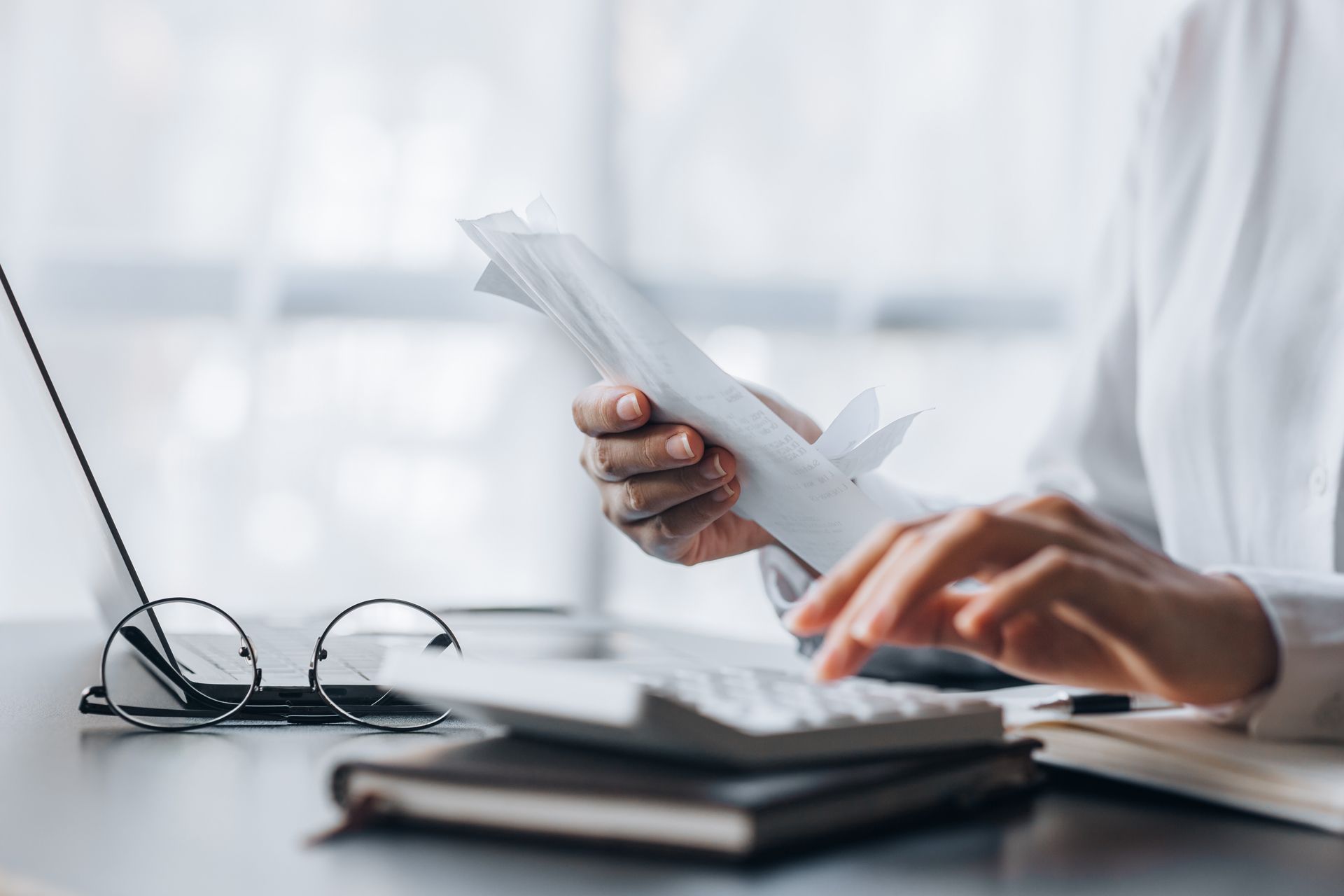 Hands counting paper bills beside eyeglasses and a calculator on a desk
