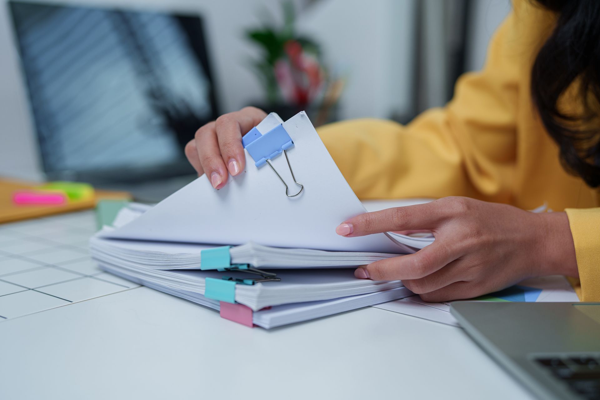 Hands flipping through a stack of papers with colorful binder clips on a desk