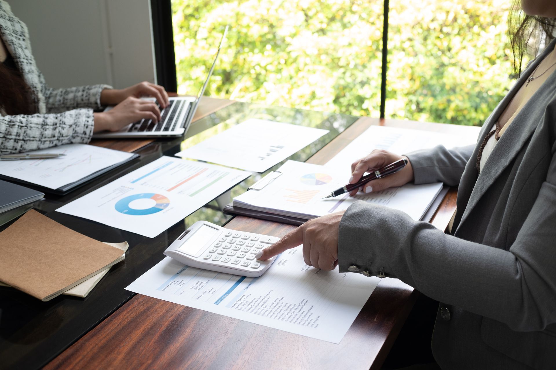Two people reviewing charts and paperwork at a desk with a calculator and laptop