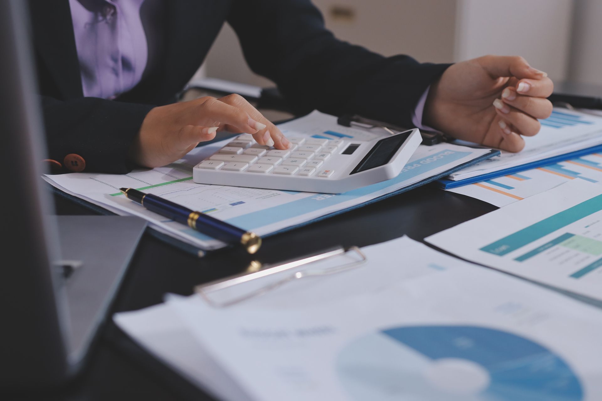 Hands using a calculator over financial charts and documents on a desk