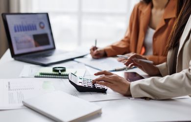 Two people reviewing documents at a desk with a laptop and calculator in an office setting
