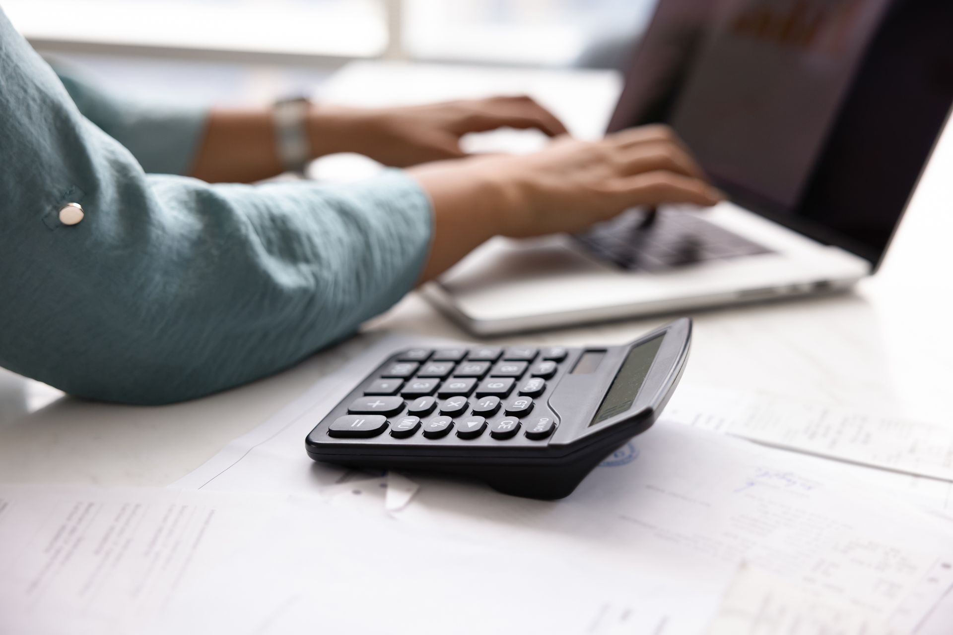 Person typing on a laptop beside a calculator on a desk