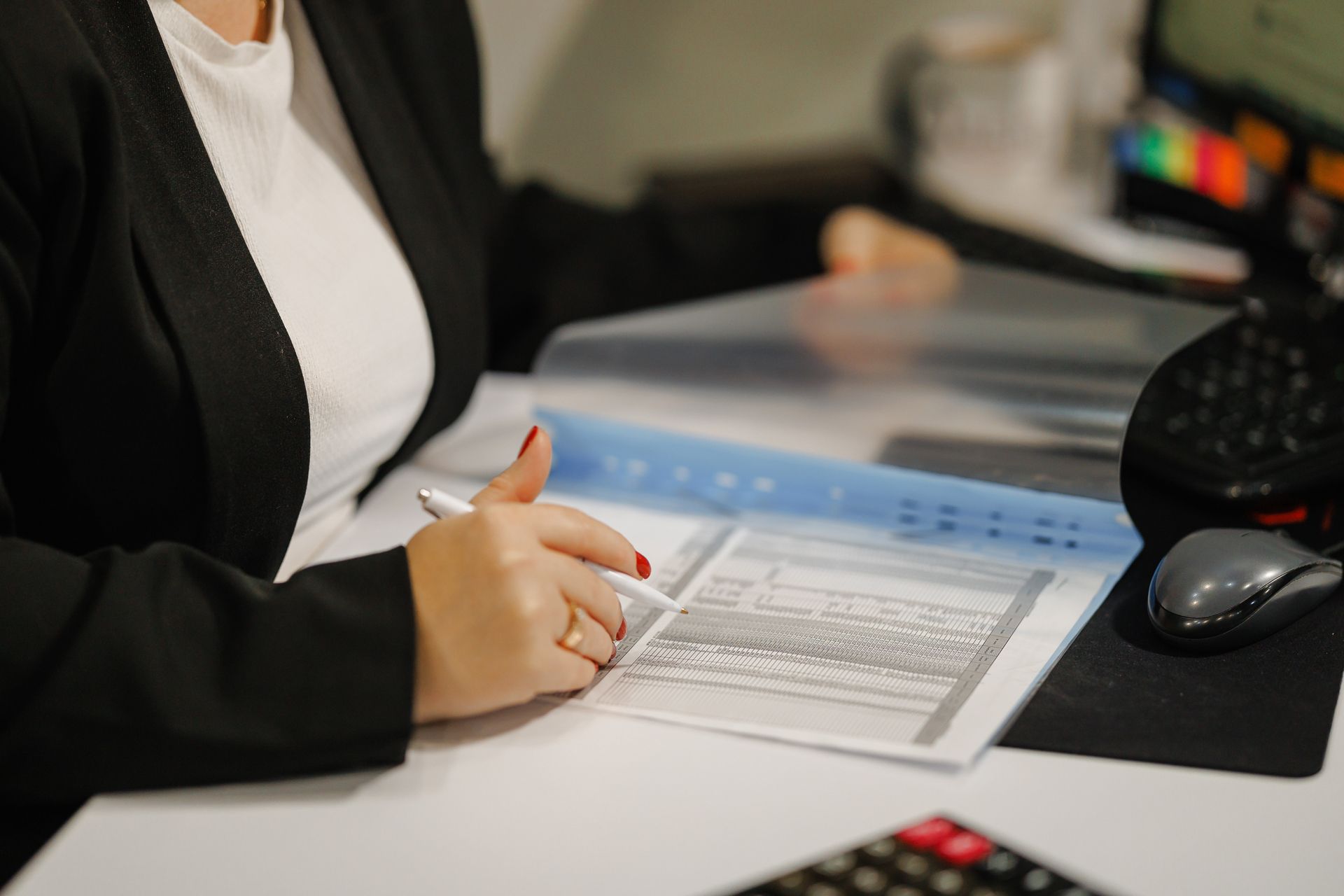 Person writing on a form at an office desk with a calculator and computer mouse nearby