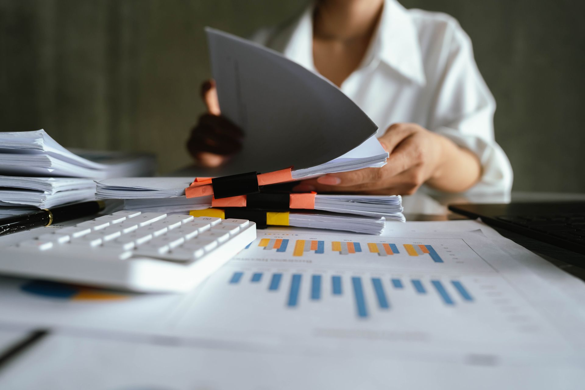 Person reviewing documents and financial charts at a desk with a calculator and laptop