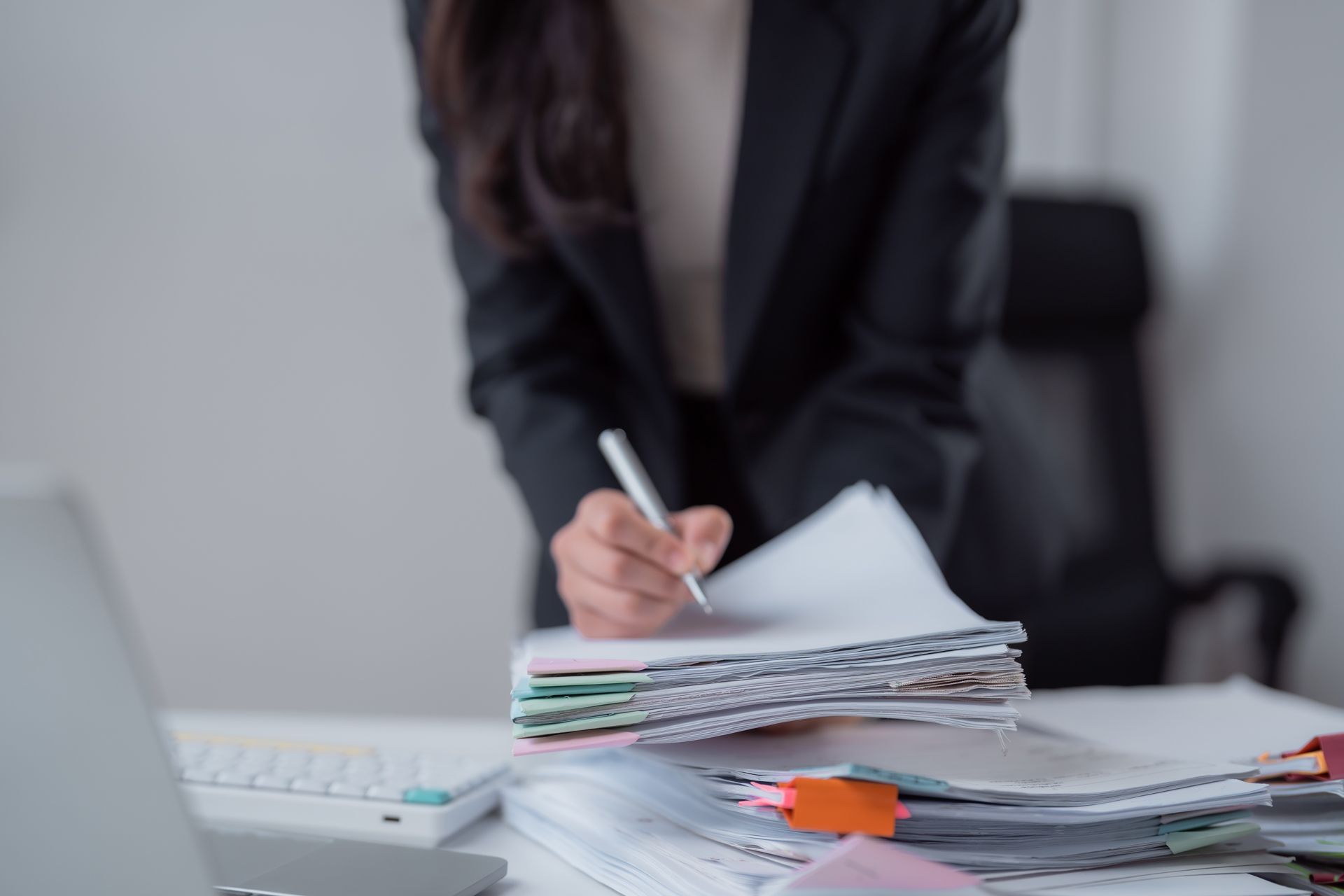 Person writing on papers at a desk with a keyboard and stacked documents