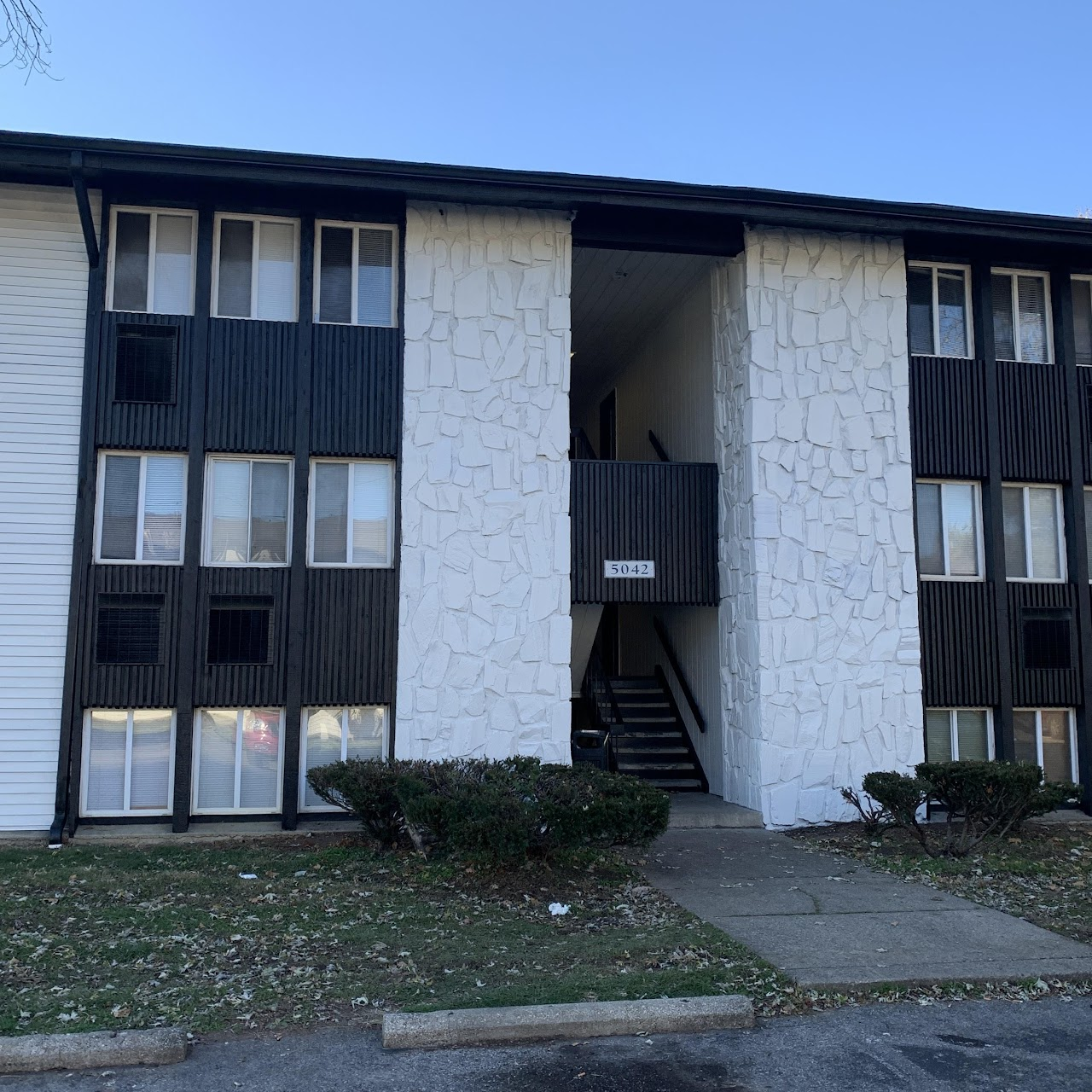 Exterior view of a three-story apartment building with black trim, white textured walls, and a stairway.