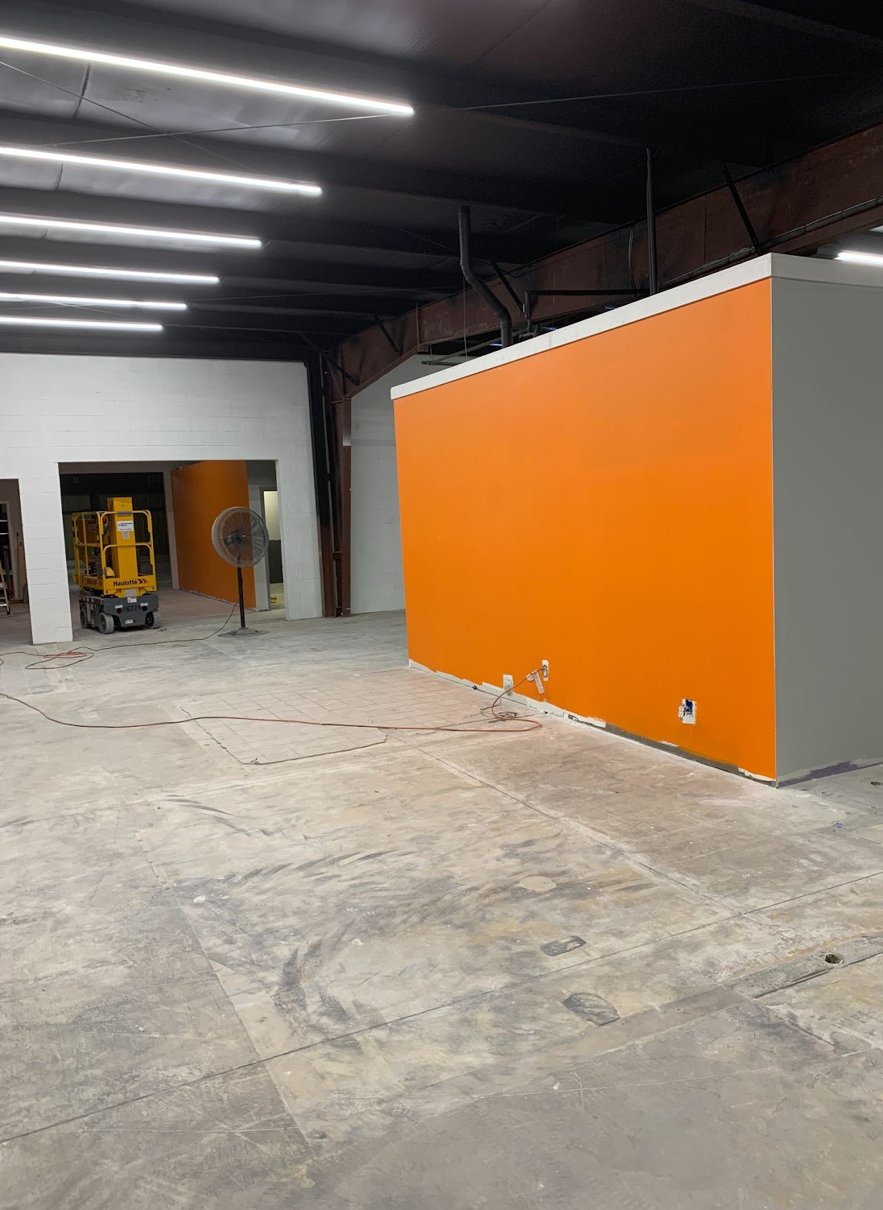 Interior of a building under construction, featuring an orange wall and concrete floor.