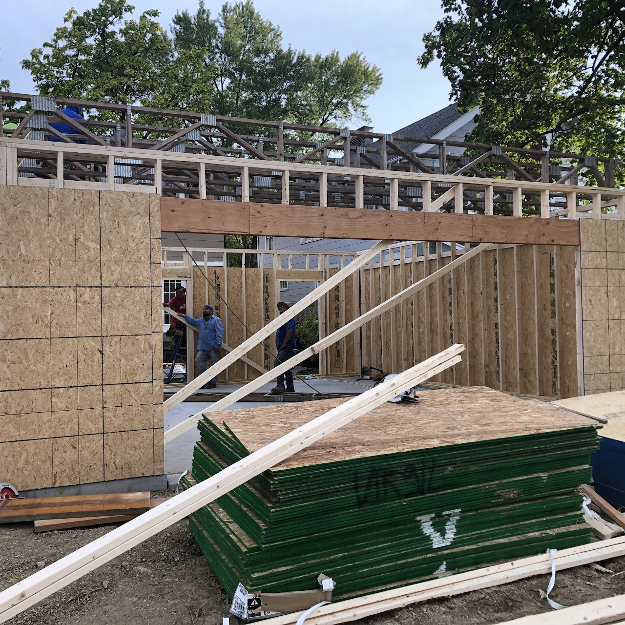 Construction site: framing for a building with wooden studs and OSB sheathing. Two workers inside the structure.