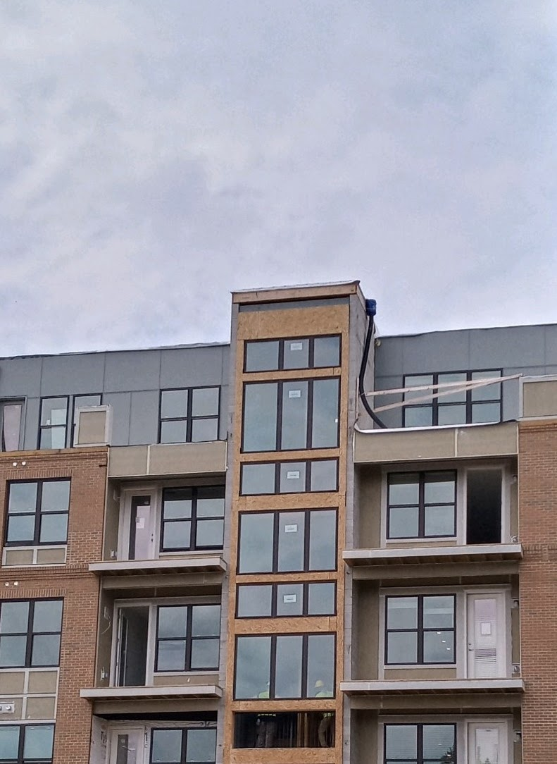 Multi-story brick building under construction with many windows against a cloudy sky.