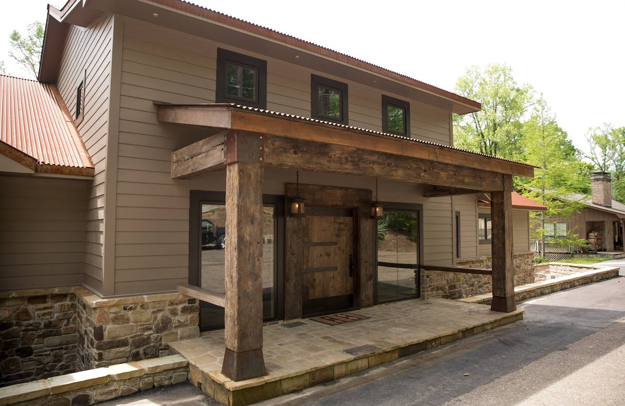 Two-story building with stone foundation and rustic wooden porch. Brown siding, red corrugated roof.