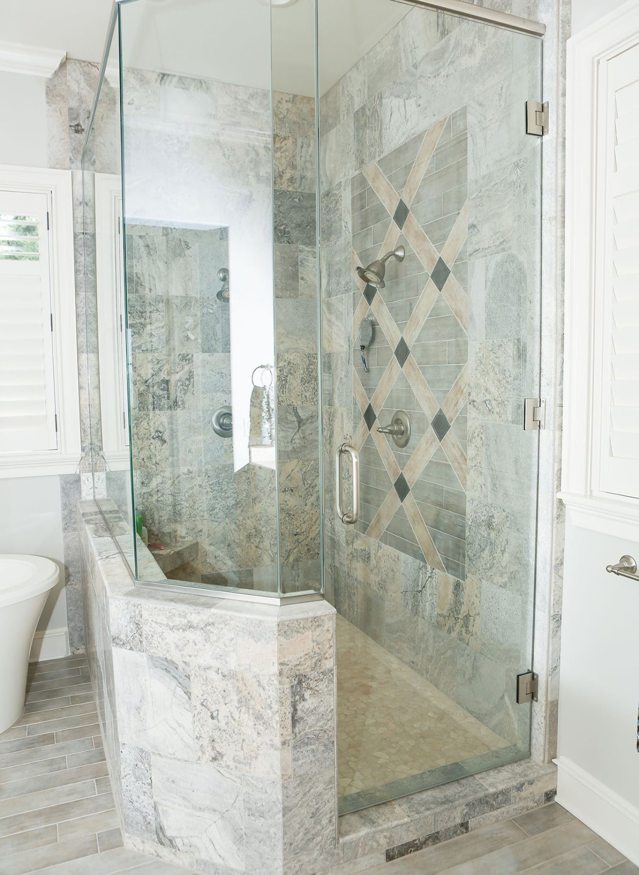 Glass shower enclosure with gray patterned tile walls and a curved marble bench.