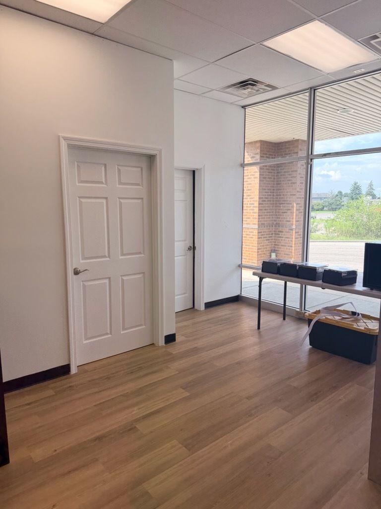 Empty office room with wood floor, white walls, a closed door, and large windows with desks.