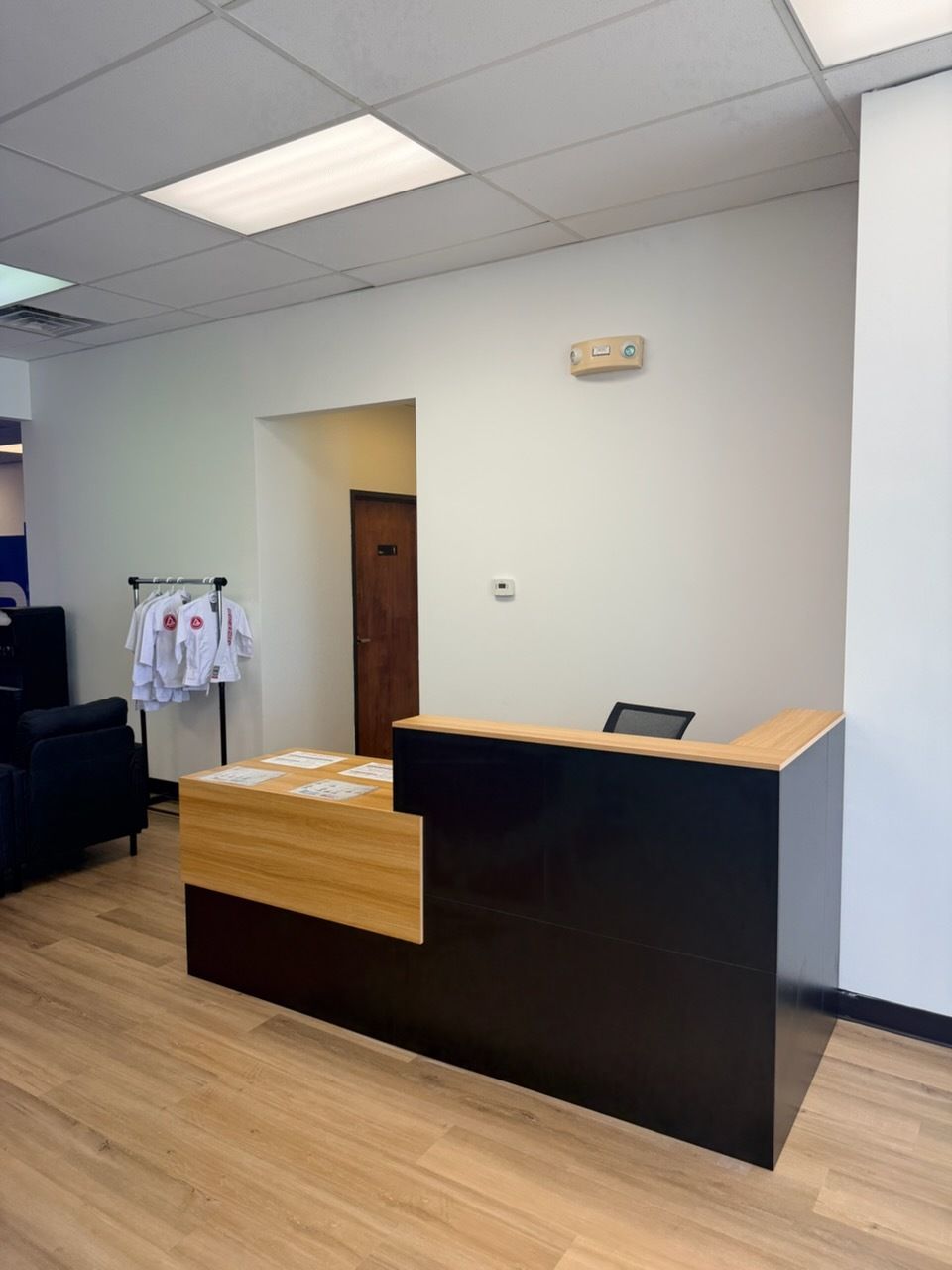 Empty office reception desk with wood-and-black counter in a bright lobby with tiled ceiling and wood floor