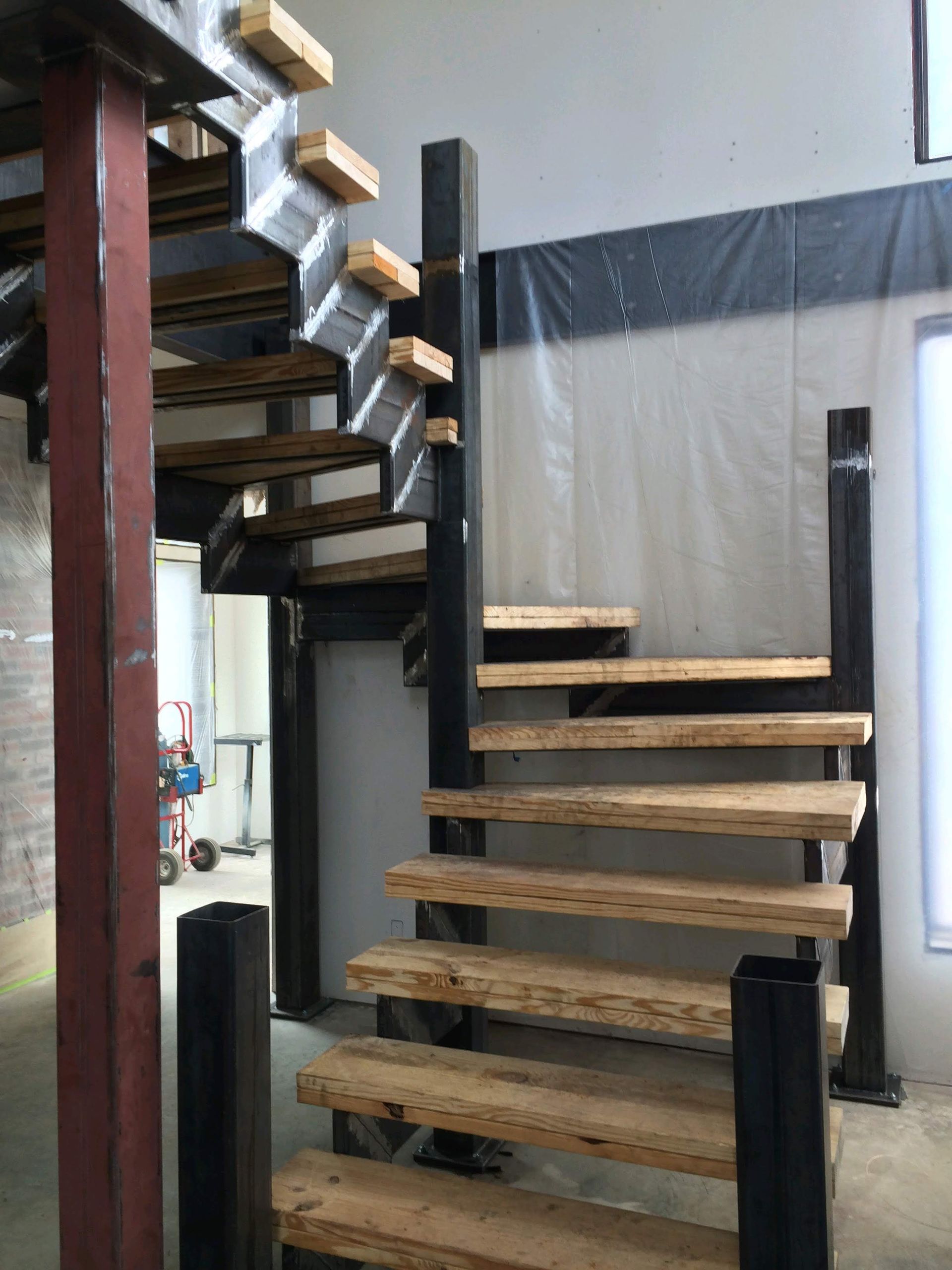 Metal and wood staircase with open treads. Black and brown tones. Industrial setting.