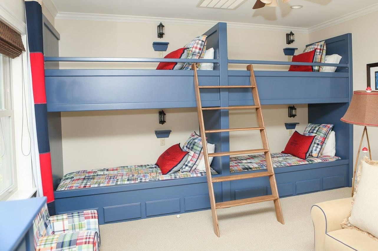 Blue bunk beds with red pillows and a wooden ladder in a brightly lit room.