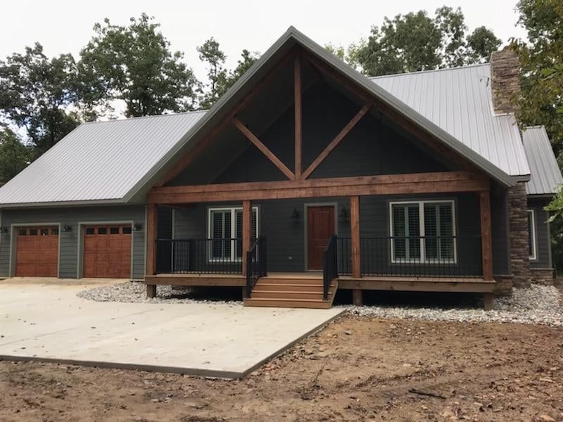 Modern gray house with brown trim and garage, metal roof, and stone chimney.