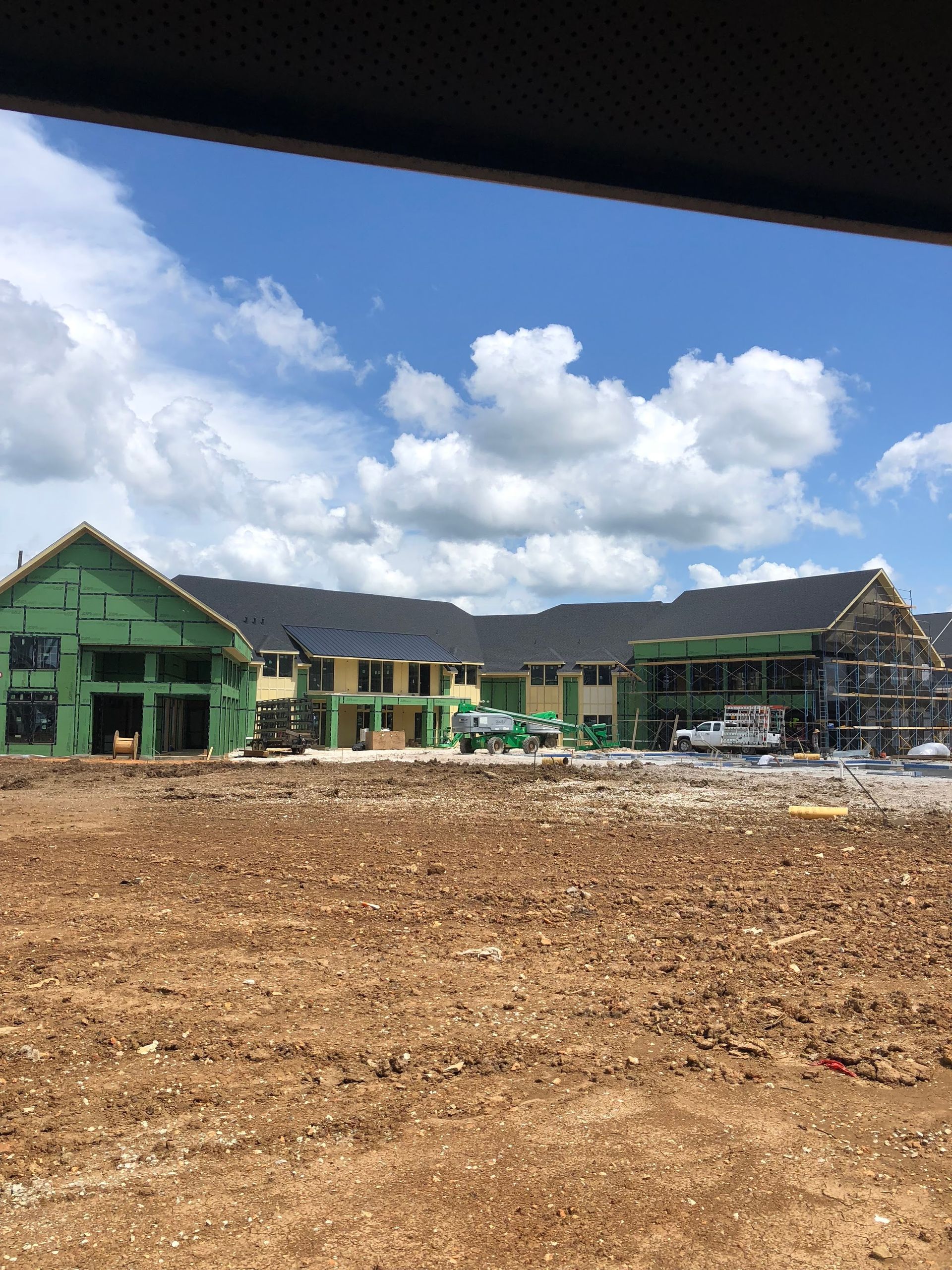 Construction site with buildings under development on a sunny day. Green siding, blue sky, and brown dirt.