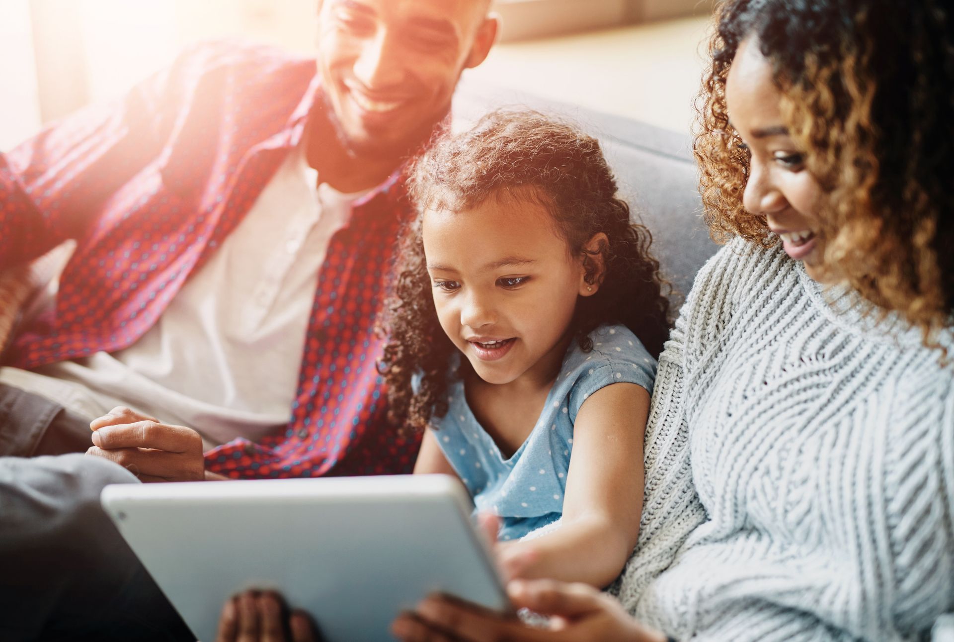 A family is sitting on a couch looking at a tablet.