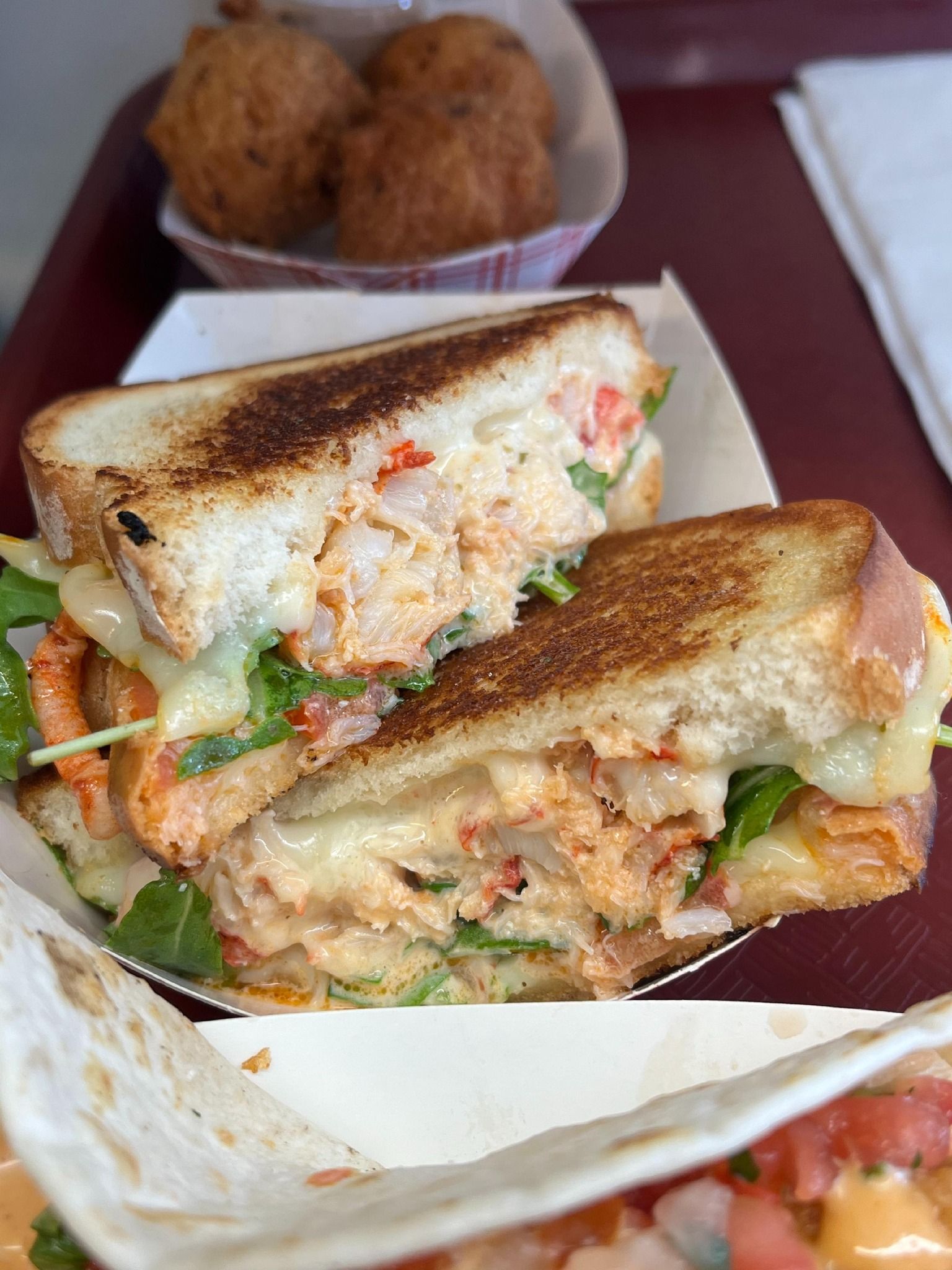 Grilled lobster sandwich on white bread, with arugula and cheese, sliced in half.