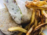 Wrap sandwich cut open, next to a pile of french fries.