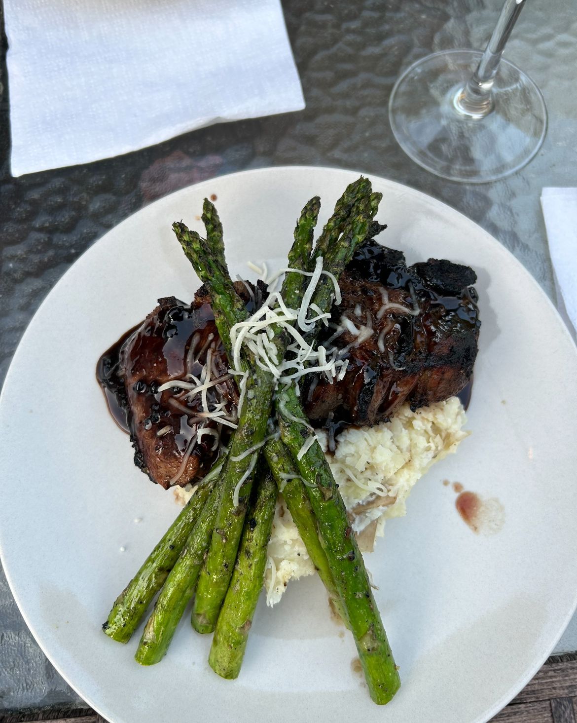 Steak with asparagus and mashed potatoes on a white plate, topped with grated cheese.