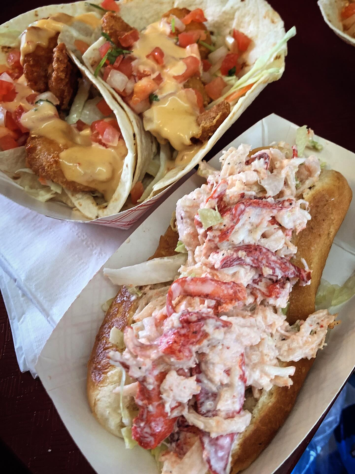 Lobster roll sandwich with fries on a silver platter. White lobster meat piled high, lettuce, and golden fries.