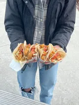 Person holding four tacos in clear wrappers.
