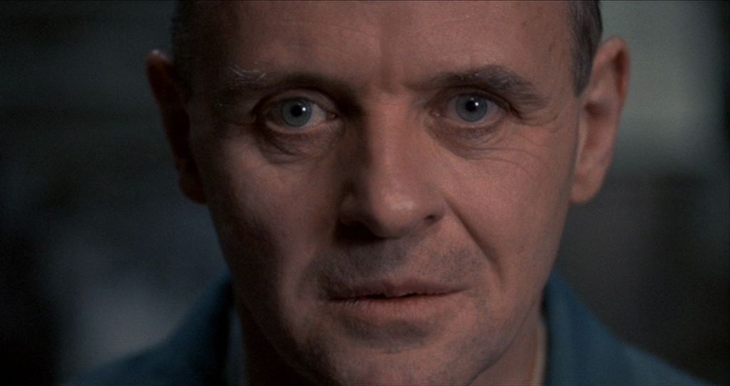 Close-up of a person with a steady, unblinking gaze and a neutral expression, captured in low-key, muted lighting.