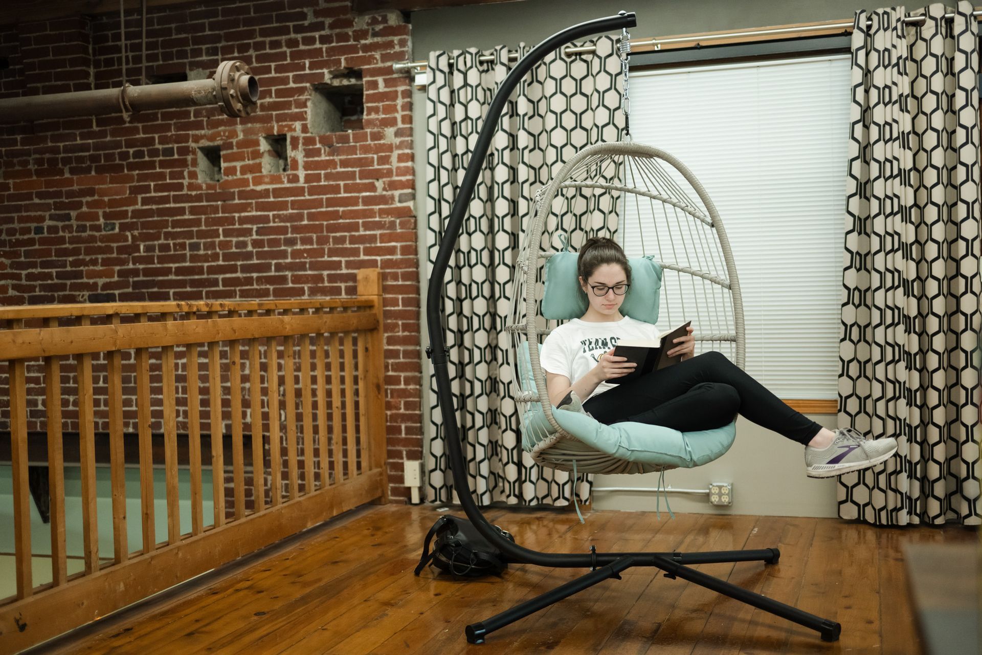 A woman is sitting in a hanging chair reading a book. A woman is sitting in a hanging chair reading a book.