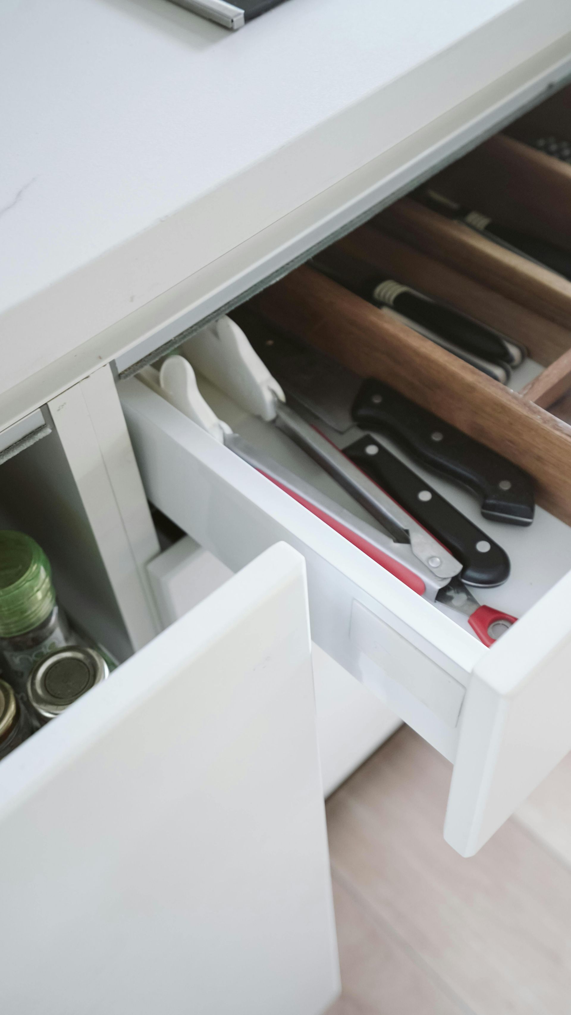 Kitchen drawer with knives and utensils in white organizers, partially open beside a countertop